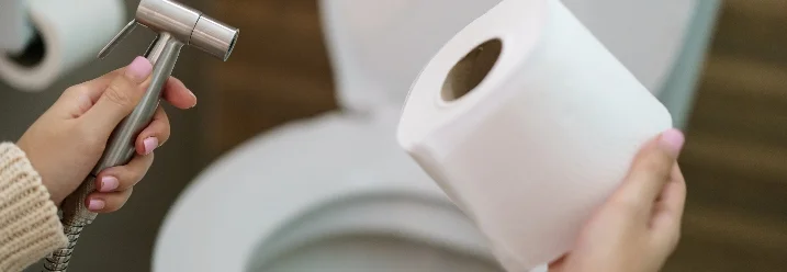 Person hält Duschkopf und Toilettenpapier